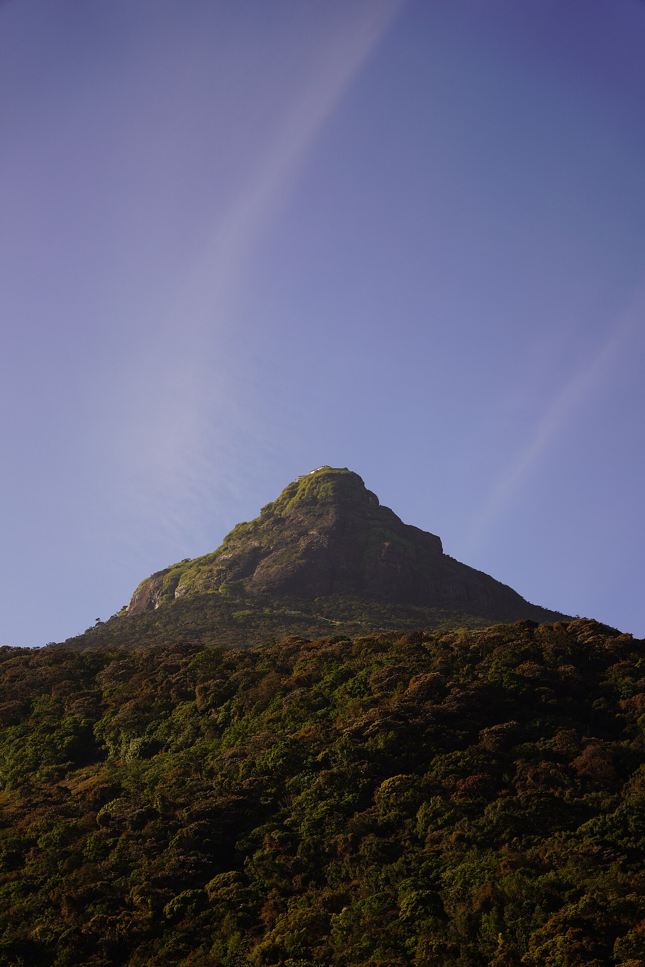 The conical summit of Adam&rsquo;s Peak rising above the hills